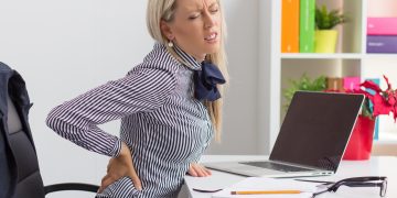 Woman having back pain while sitting at desk in office