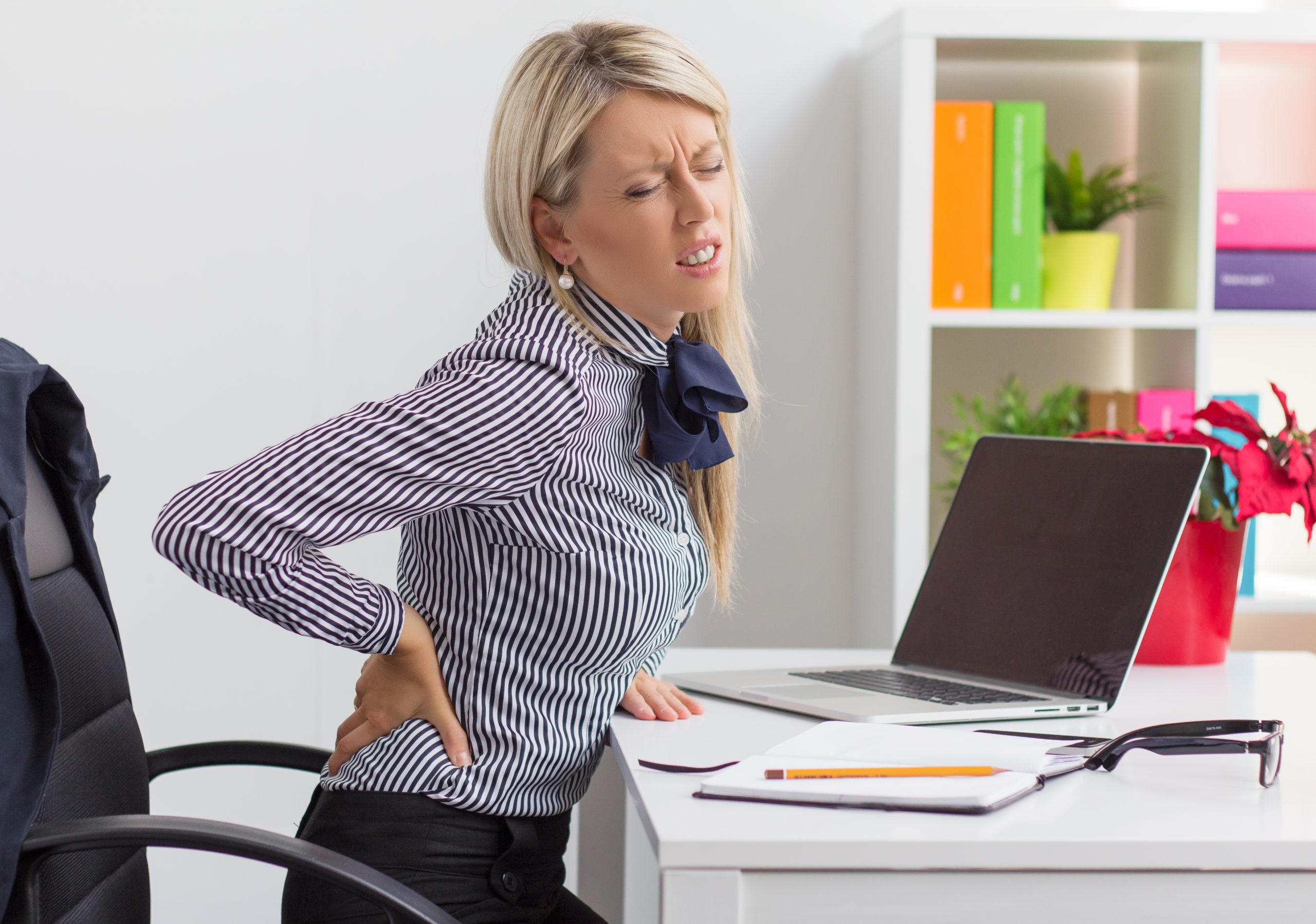 Woman having back pain while sitting at desk in office